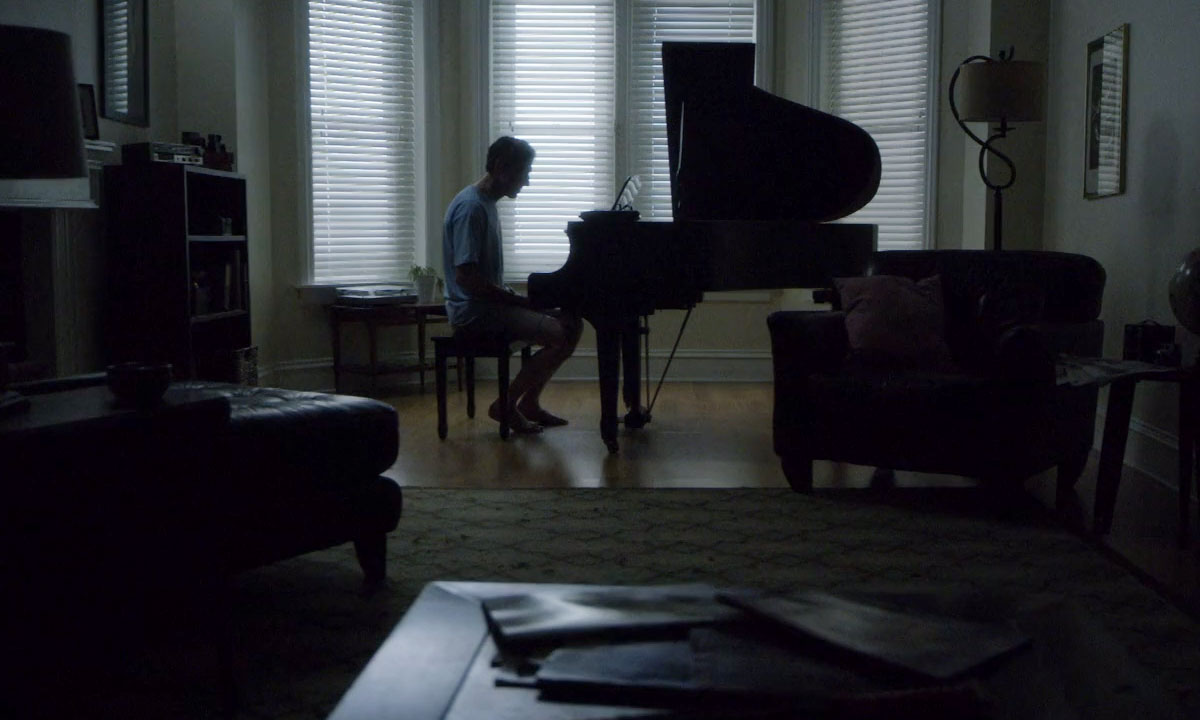 man infront of a piano  in his gloomy living room